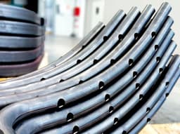 Curved metal pipes with uniformly spaced holes, arranged in a stack, used in industrial or structural applications.