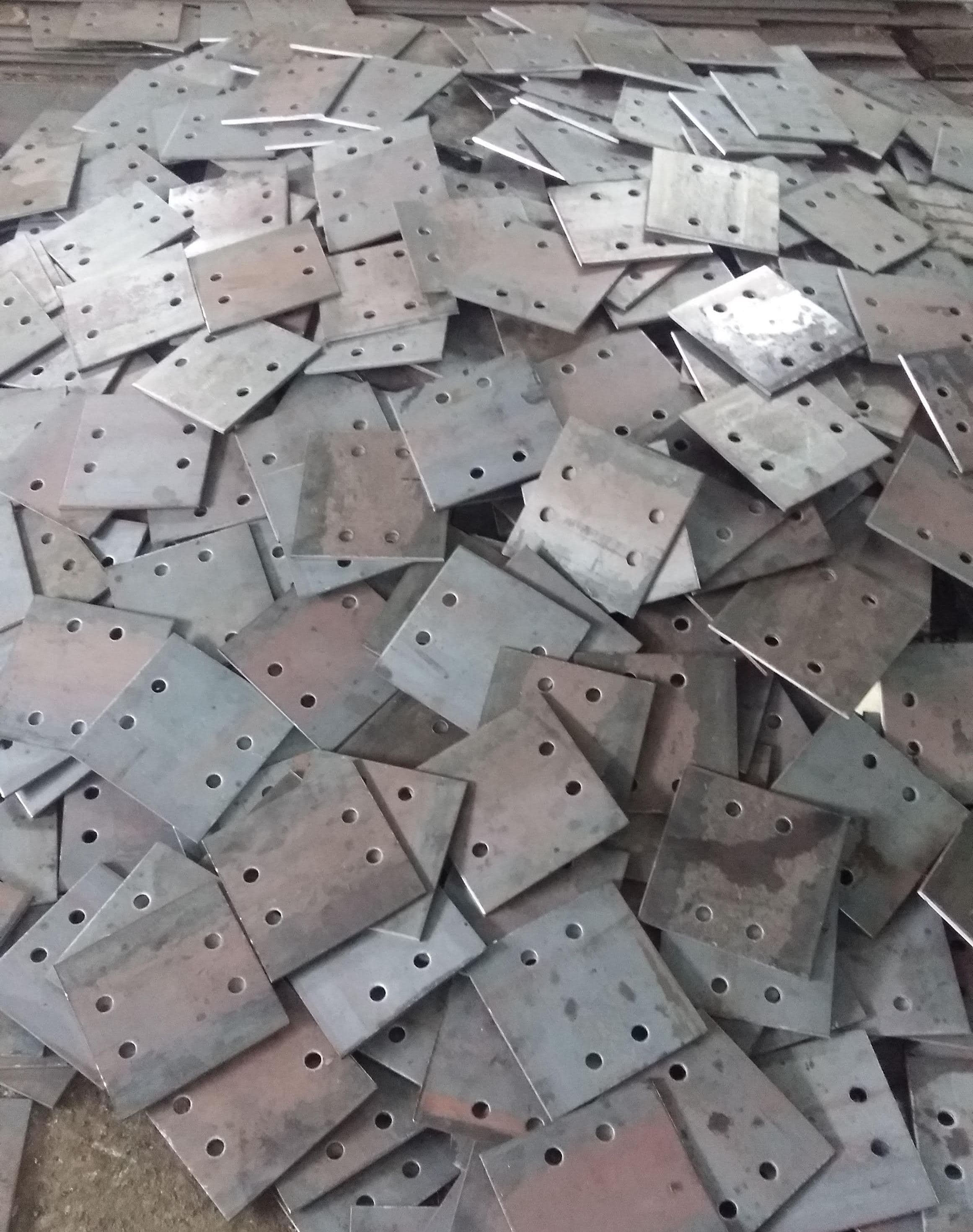 Stack of metal base plates with bolt holes, used in construction and infrastructure applications.