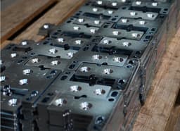 Stacked precision-machined metal plates with countersunk holes, used in defense and aerospace components.