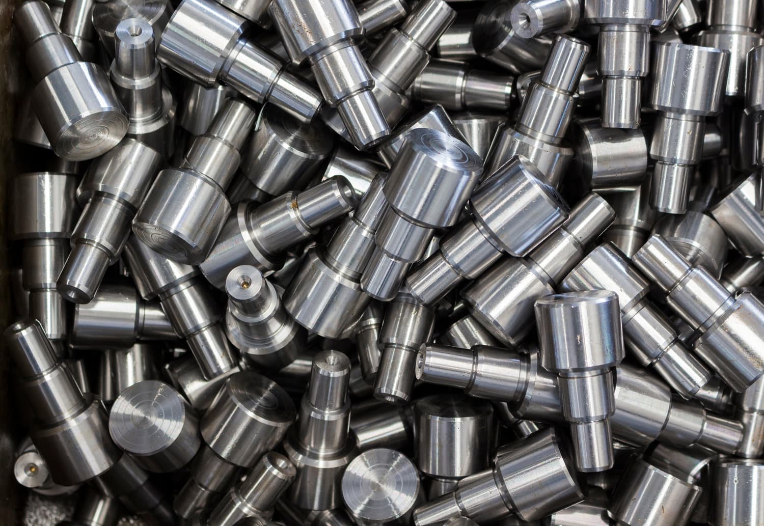 Pile of identical cylindrical screw-machined metal components used in high-volume industrial manufacturing.