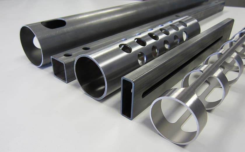 Assorted metal tubes and profiles with precision laser-cut patterns including circular holes, slots, and spiral designs, demonstrating advanced tube laser cutting capabilities.